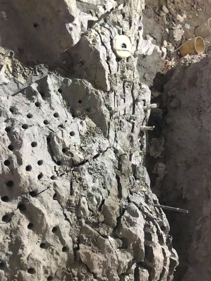 Close-up of a roughly hewn, light-grey stone wall with numerous drilled holes and a crack.