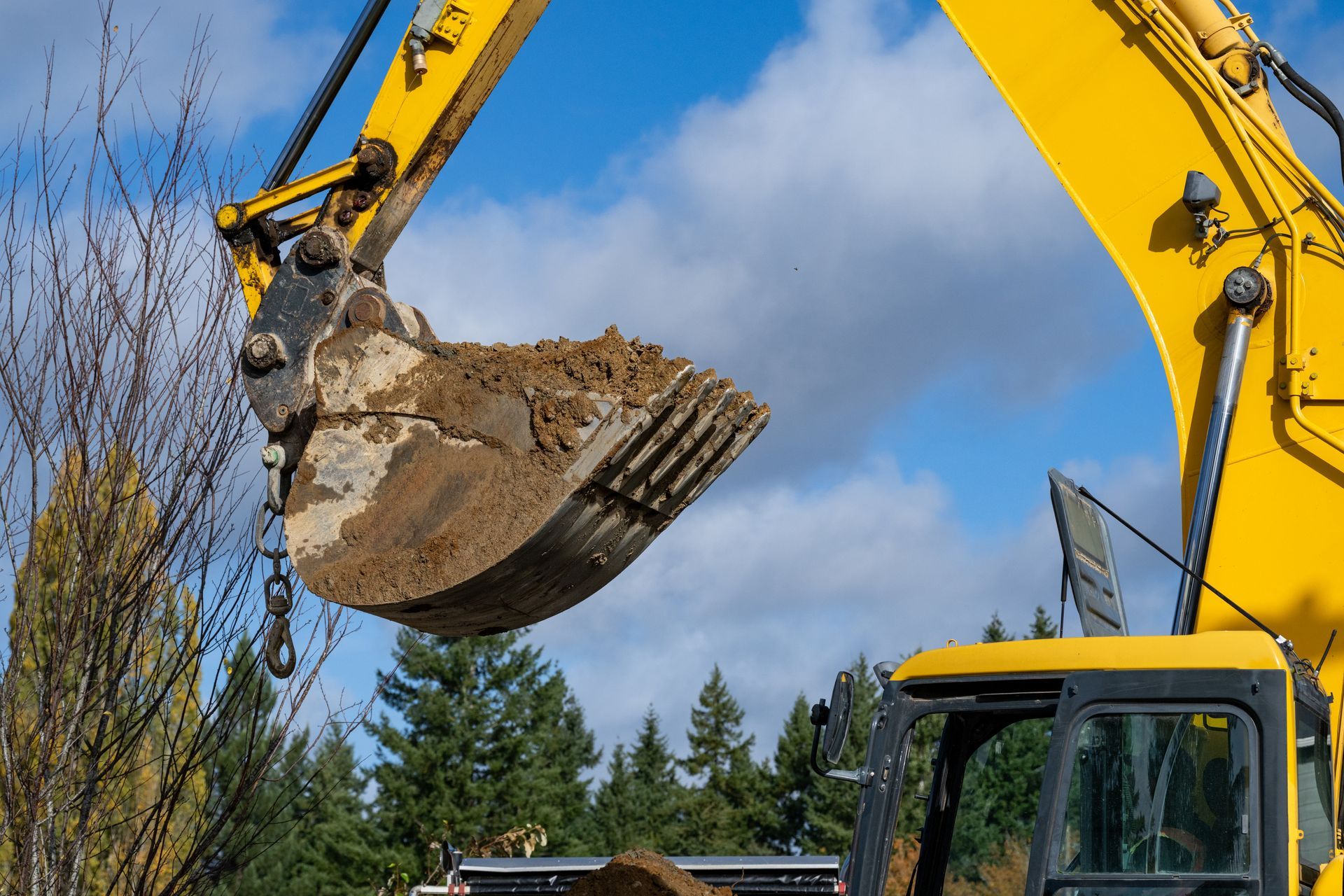 A yellow excavator hydraulic bucket lifting dirt at a construction site. A yellow excavator hydraulic bucket lifting dirt at a construction site.