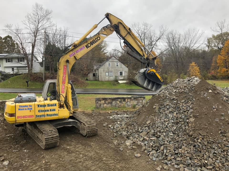 Yellow excavator dumping gravel onto a pile on a construction site.