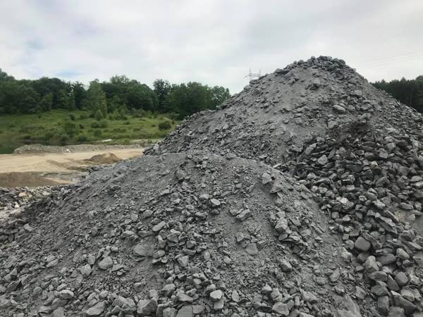 Pile of gray gravel on a construction site; trees and overcast sky in the background.