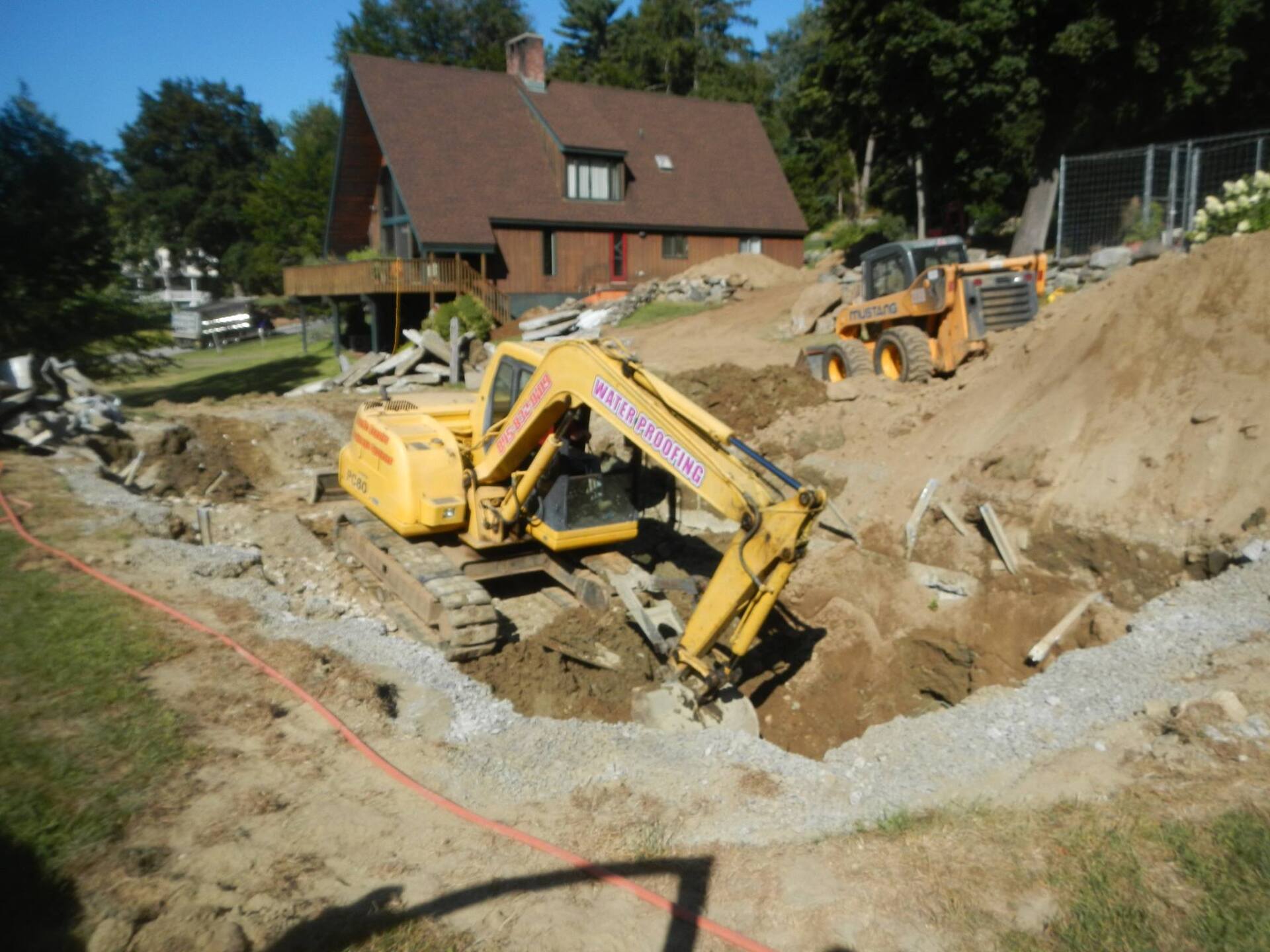 Yellow excavator digging on a residential construction site; a small tractor is in the background.