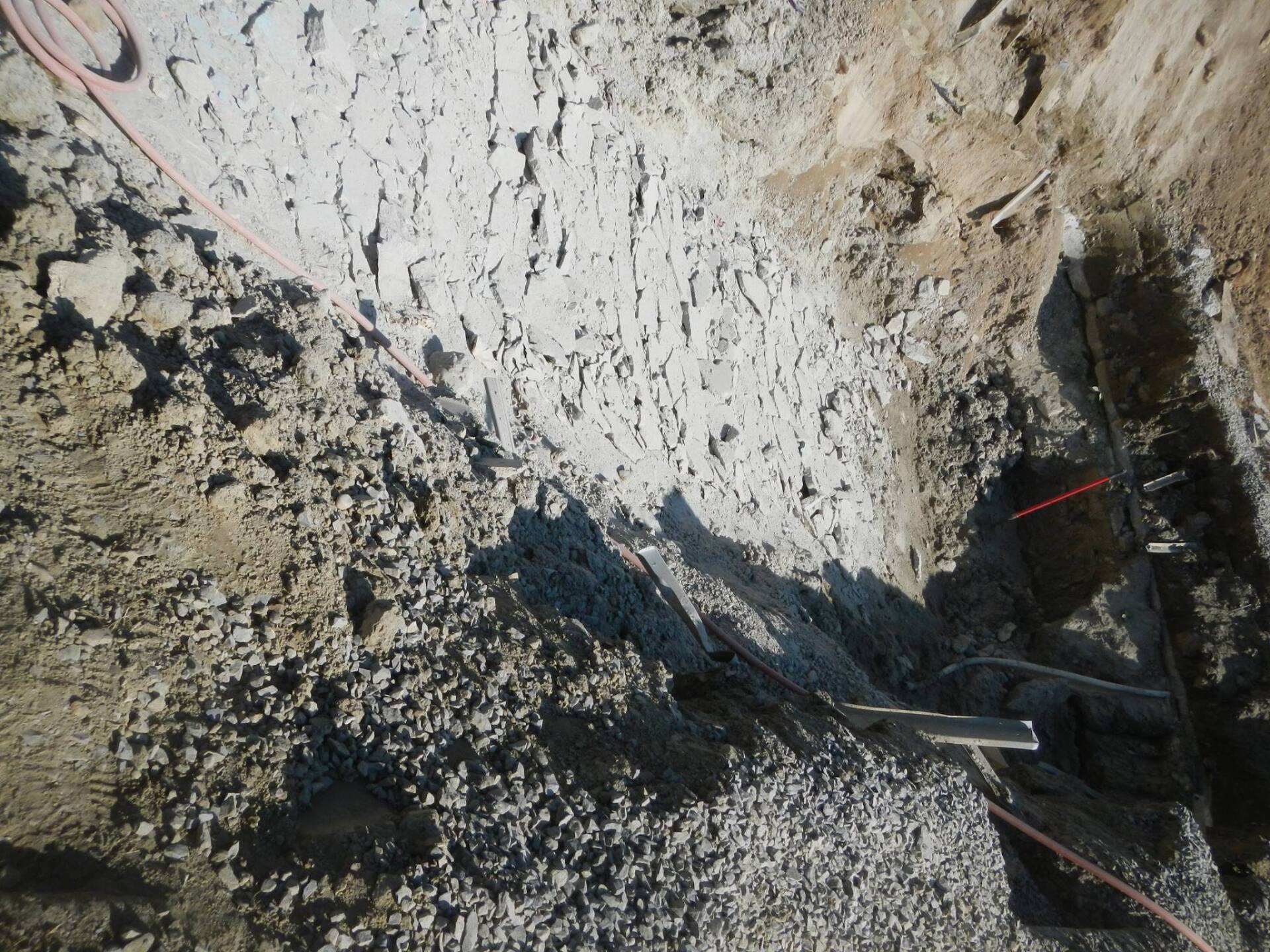 Excavation pit with light gray and brown soil, red wires, and a metal beam.