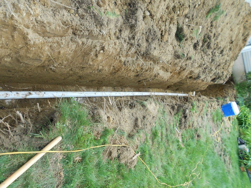 Trench dug in soil with a white pipe running through it, on green grass.