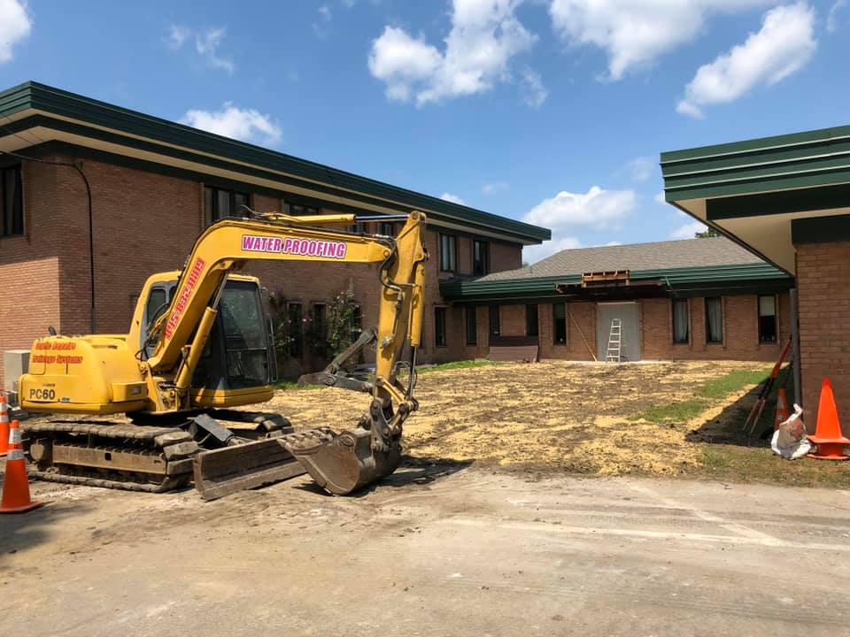 Yellow excavator in front of a brick building during construction on a sunny day.