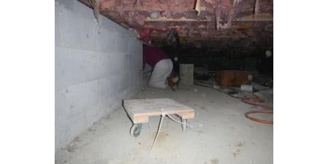 Person crouched in crawlspace with wooden platform, blocks, and insulation.