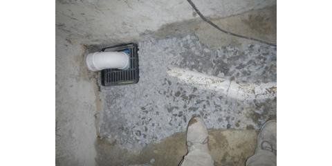 A drain with a white pipe in a concrete area with gray debris and a person's boots visible.