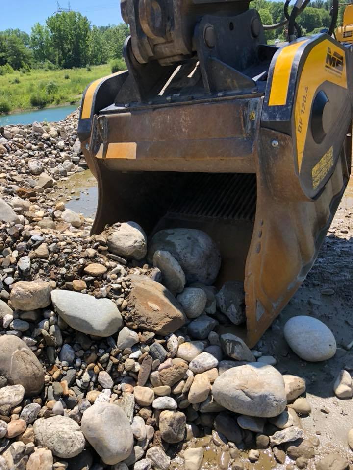 A rock sifter on a construction site sorting stones; yellow machine, gravel, water, and blue sky in the background.