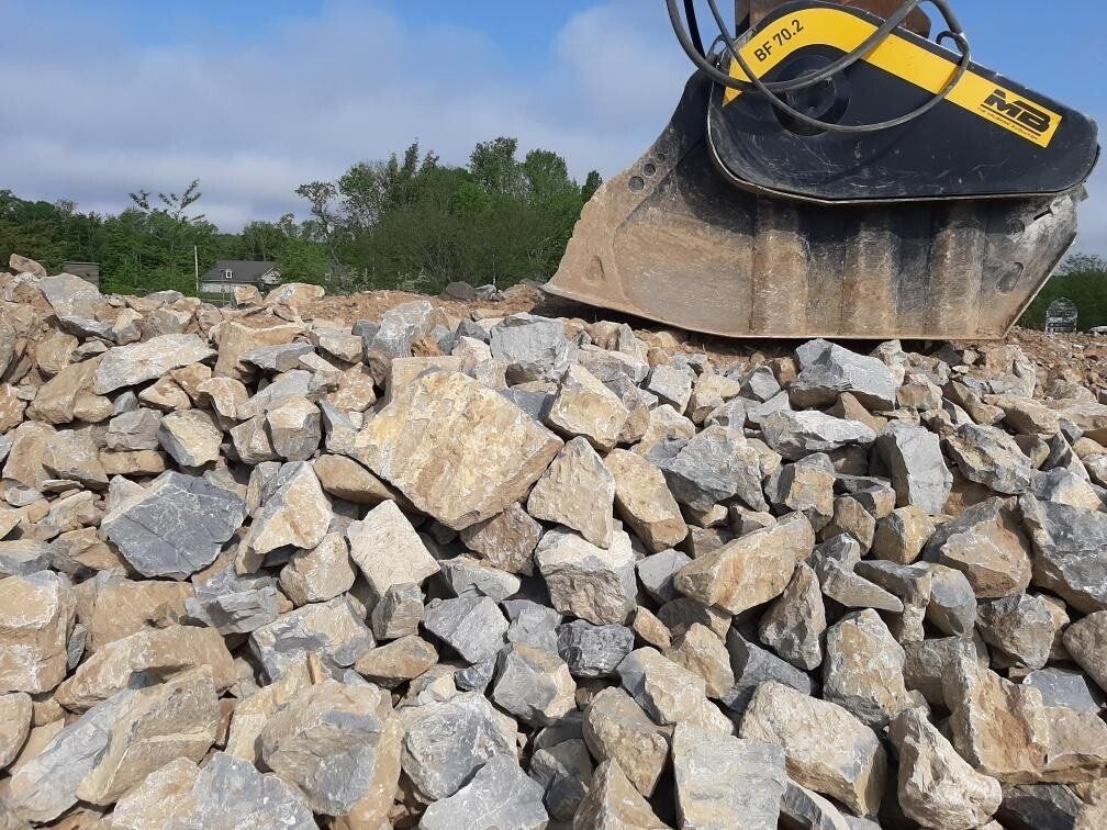Excavator bucket over a pile of broken rocks, construction site under a blue sky.