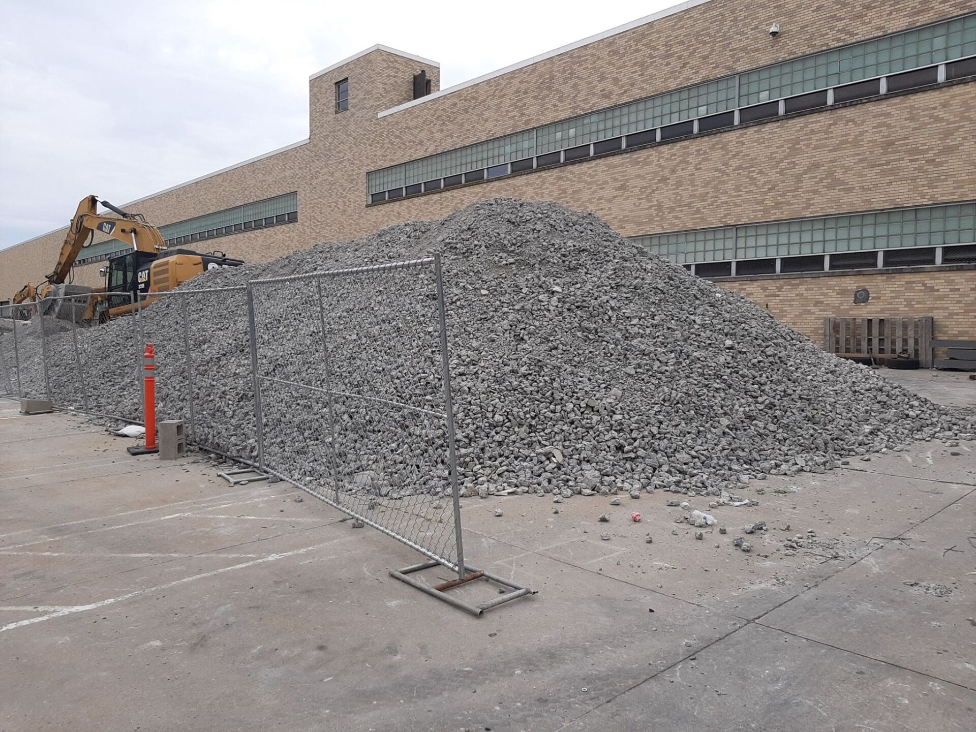 Construction site with a large pile of rubble behind a barrier and an excavator next to the building.