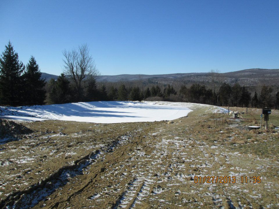 A snow-covered clearing on a hill with bare trees, mountains, and a clear blue sky.