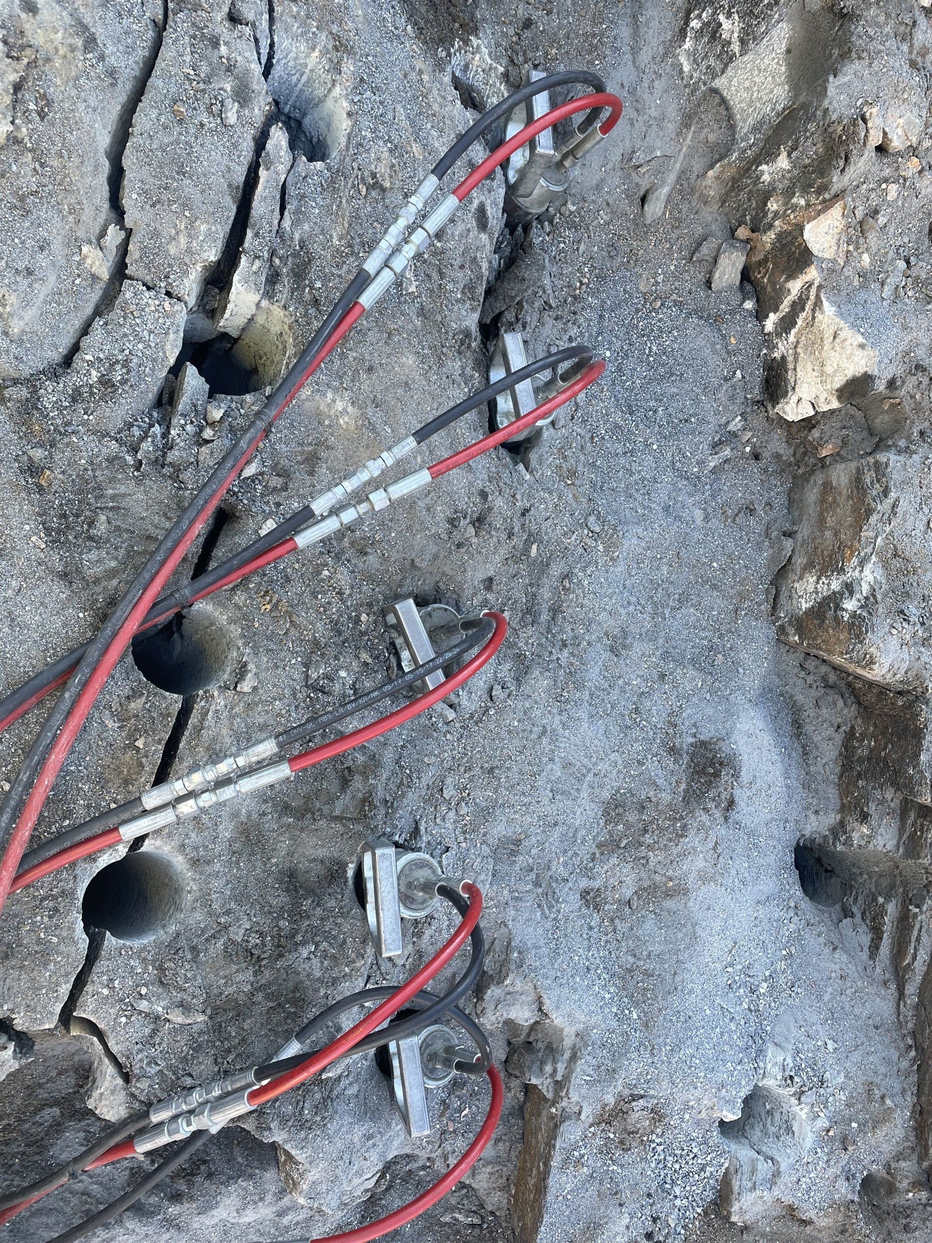 Close-up of a damaged concrete wall with wires and metal clips attached, holes drilled into the surface.