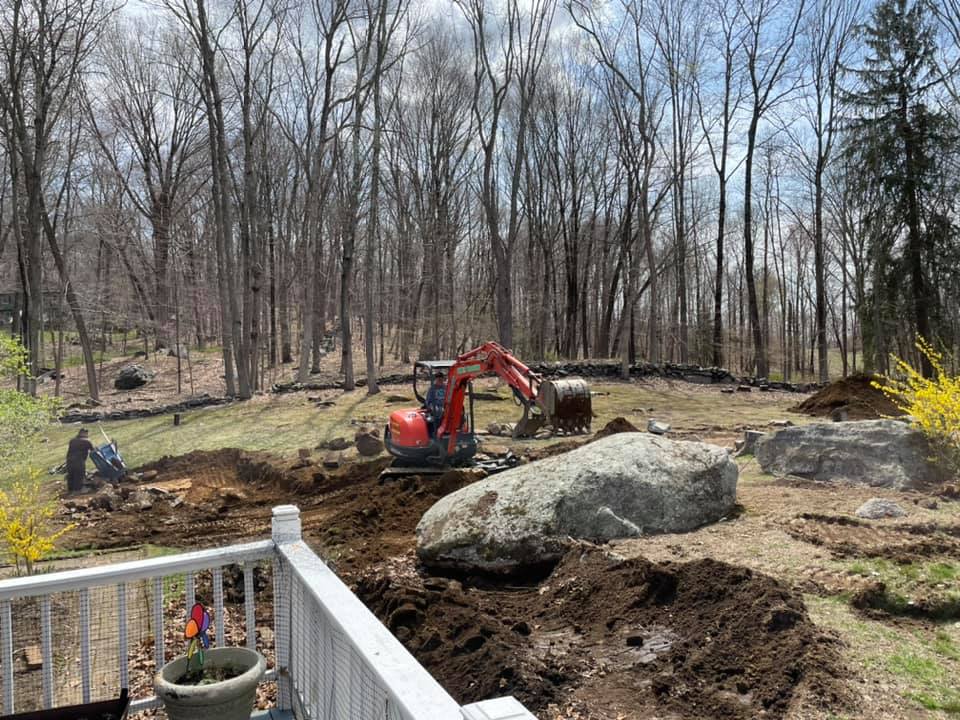 Construction site with a small excavator, large boulders, and a person working.