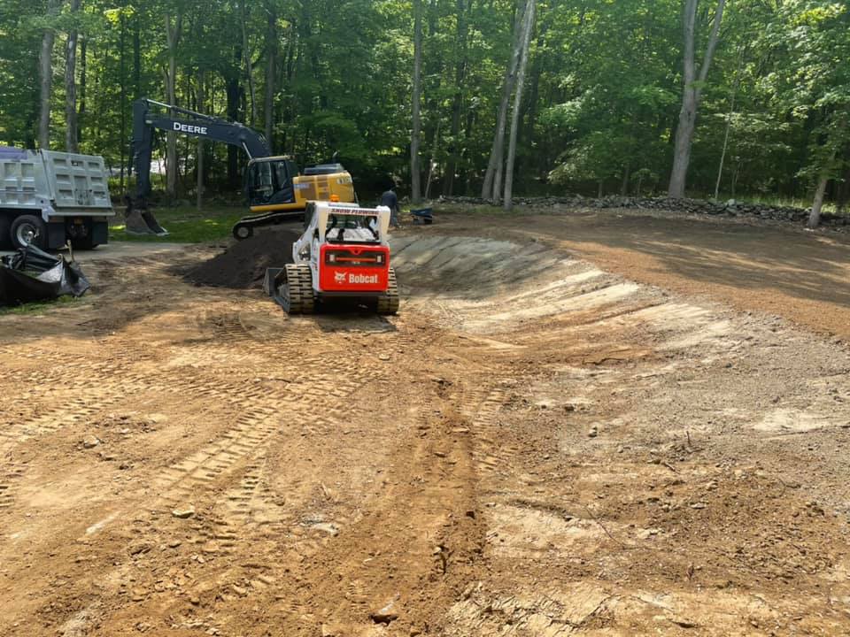 A red Bobcat skid-steer loader operating on a dirt construction site with other heavy equipment.