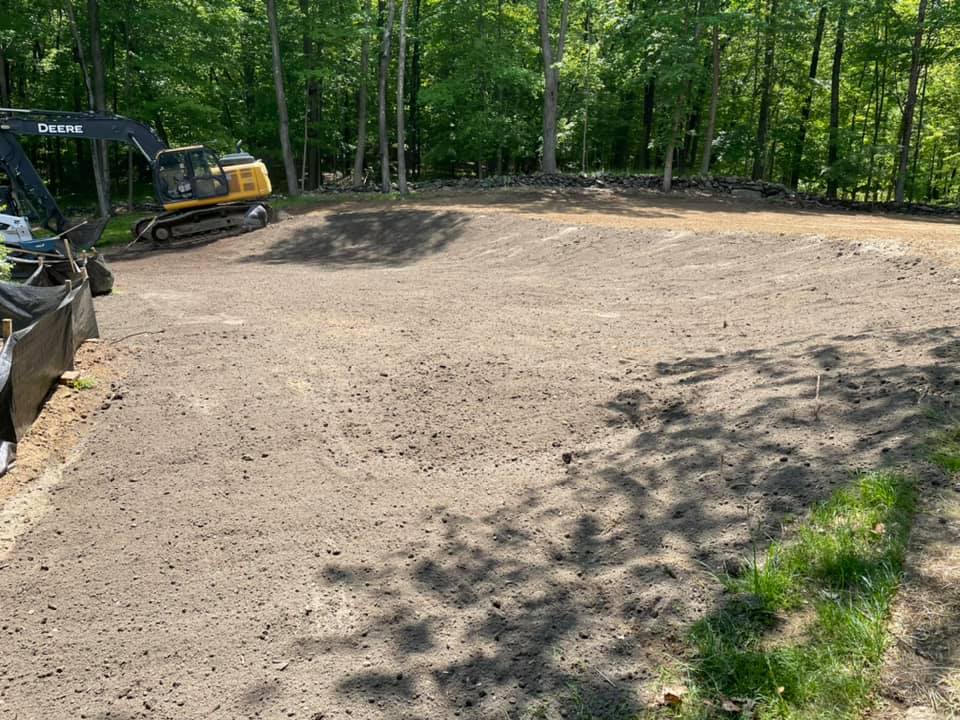 Cleared lot with heavy equipment, soil, and trees in background.