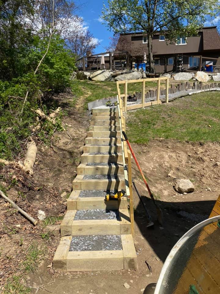 Staircase built on a hillside. Wooden steps with light grey gravel insets. Handrail and a house in the background.
