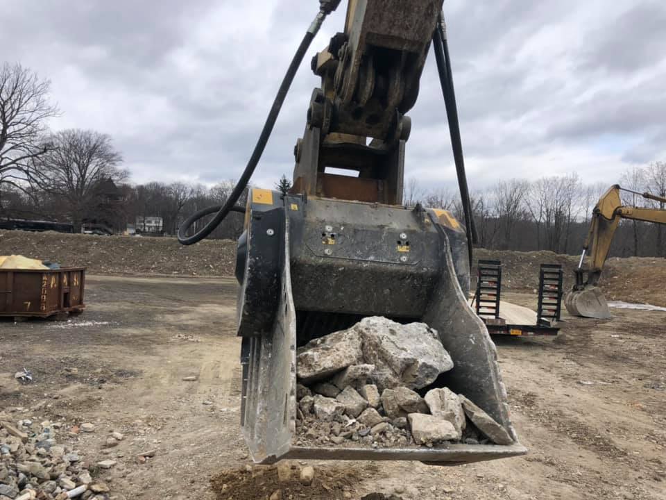 Excavator bucket holding rocks at a construction site on a cloudy day.