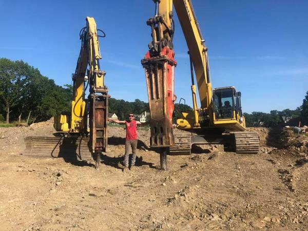 Person stands between two yellow excavators with demolition attachments on a construction site.