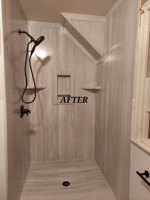 Newly renovated shower with light wood-look panels, black fixtures, built-in shelves, and a recessed niche.