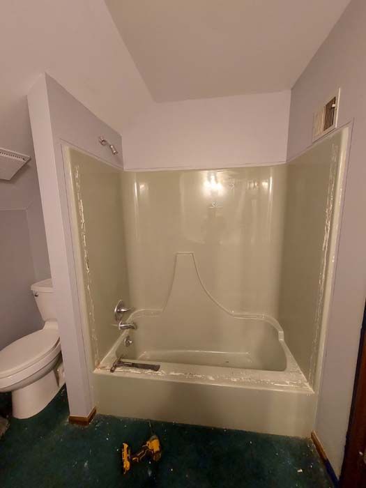 Bathroom with a light green tub and shower surround, a toilet, and purple walls.