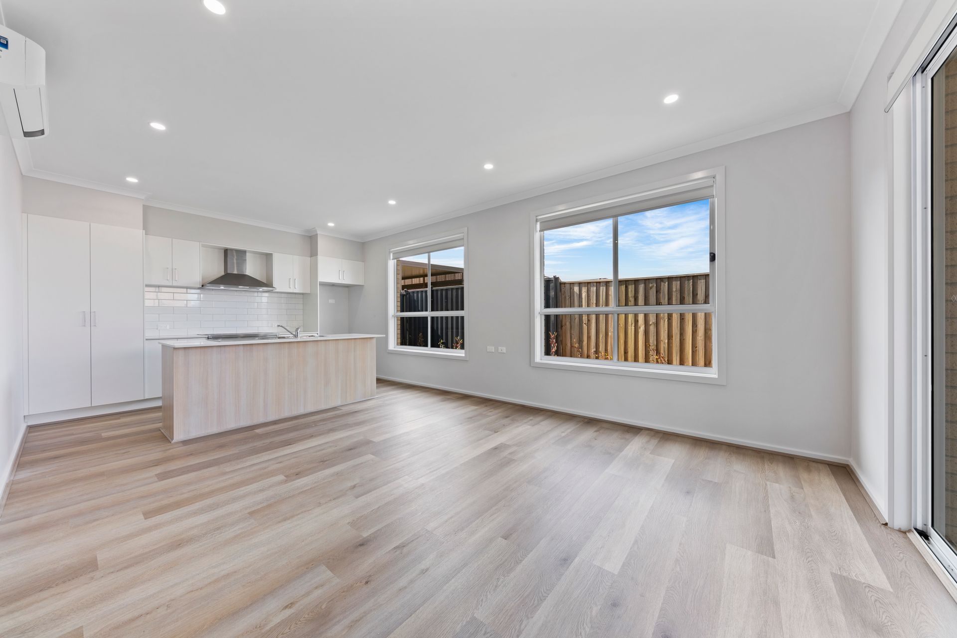 An empty living room with hardwood floors and a kitchen.