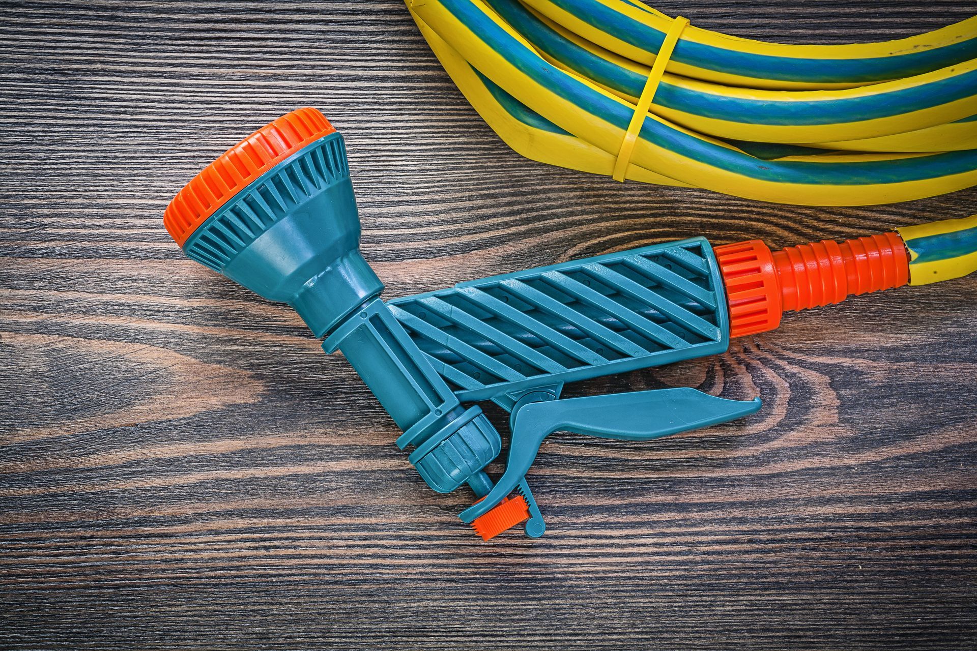 A garden hose coil, a water hand spray gun on a wooden board, showcasing agricultural equipment.