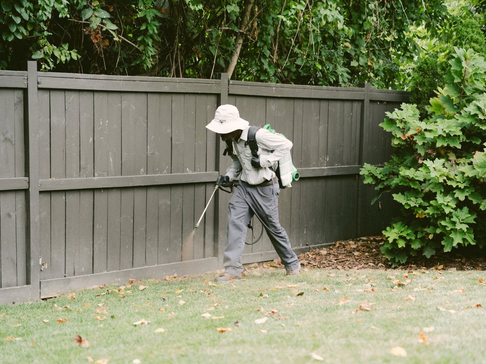 Person using a string trimmer along a wooden fence in a grassy yard