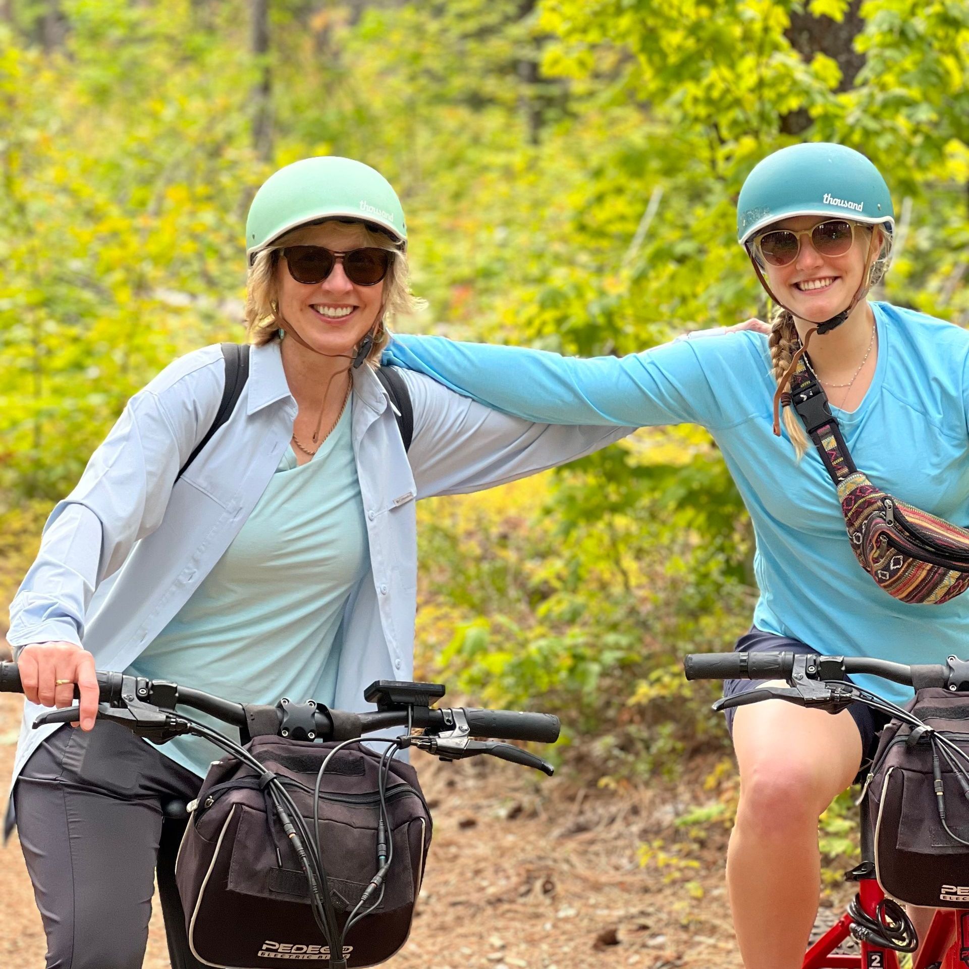 Two women are standing next to each other on bicycles in the woods.