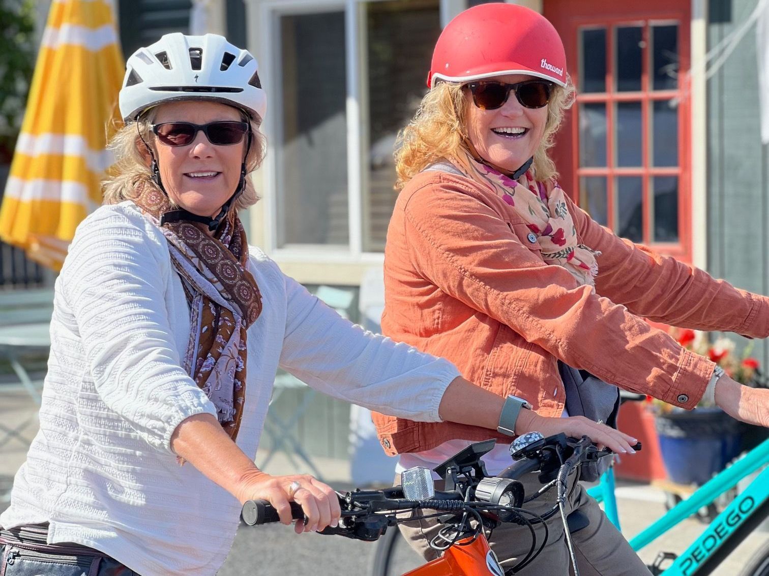 Two women are riding bicycles in front of a building.