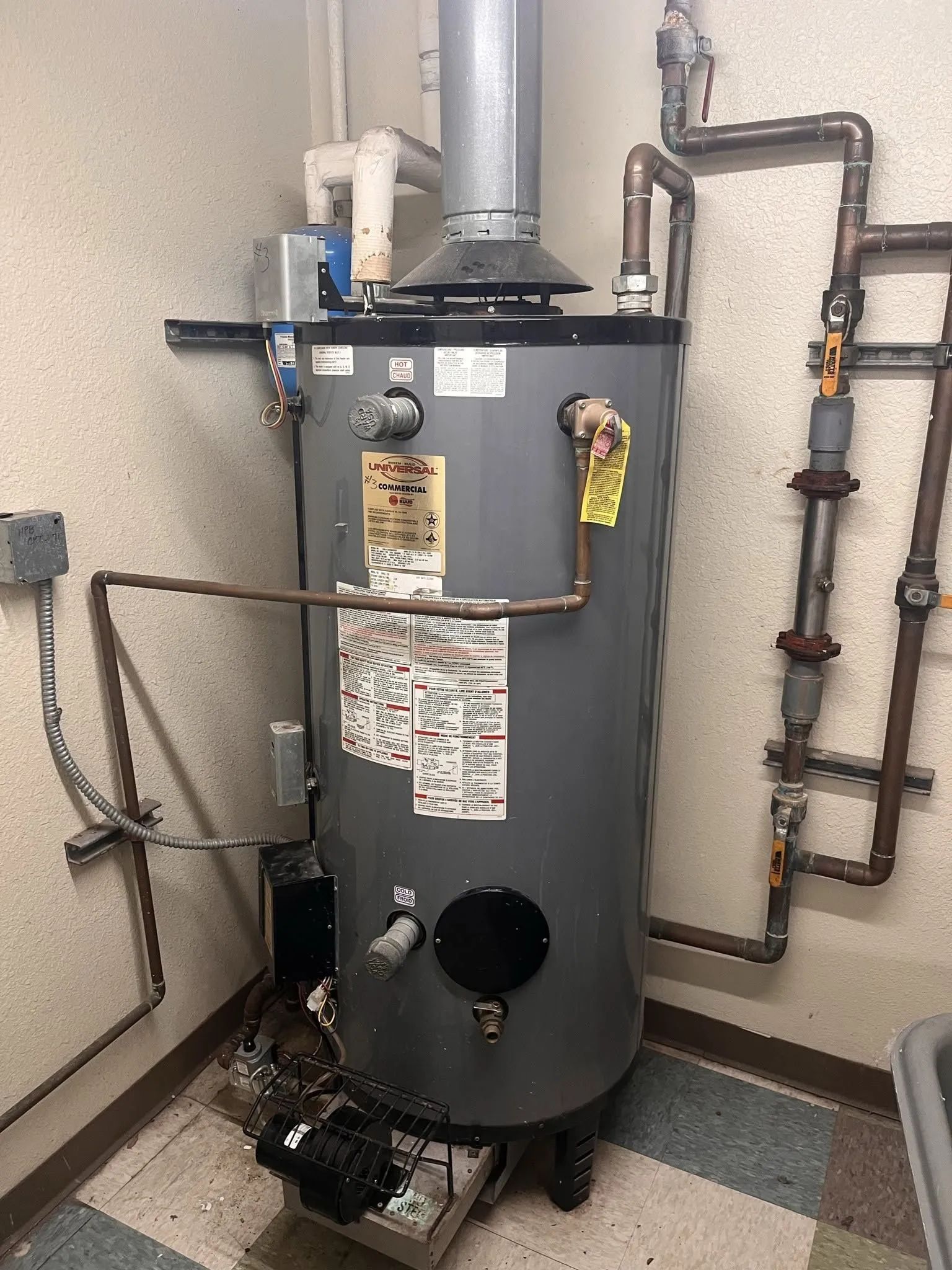 Tall gray water heater with pipes and valves in a utility room, with a vent pipe on top.