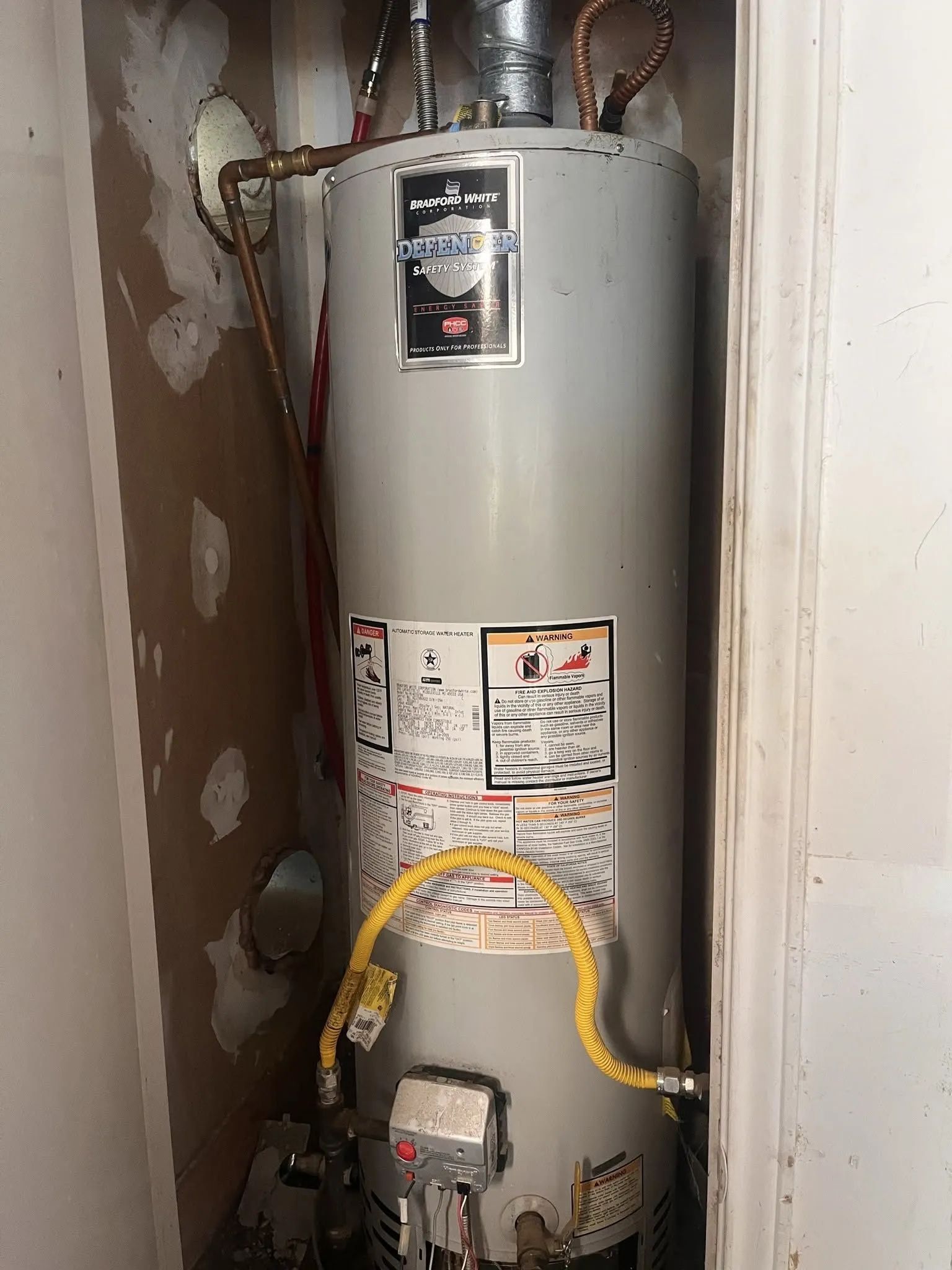Water heater in a narrow closet with visible pipes and a yellow flexible gas line.