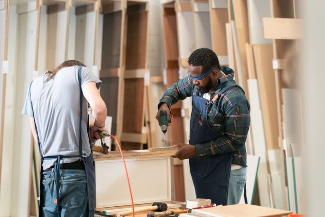 Two workers in a woodworking shop measuring and cutting a wooden board