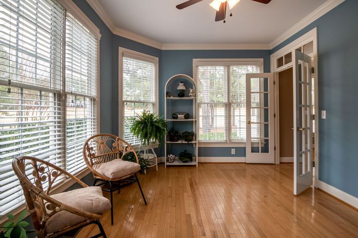 Bright sunroom with blue walls, wicker chairs, hardwood floor, and large windows with blinds.