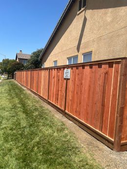 Red stained wooden fence alongside a green lawn and beige house under a blue sky.