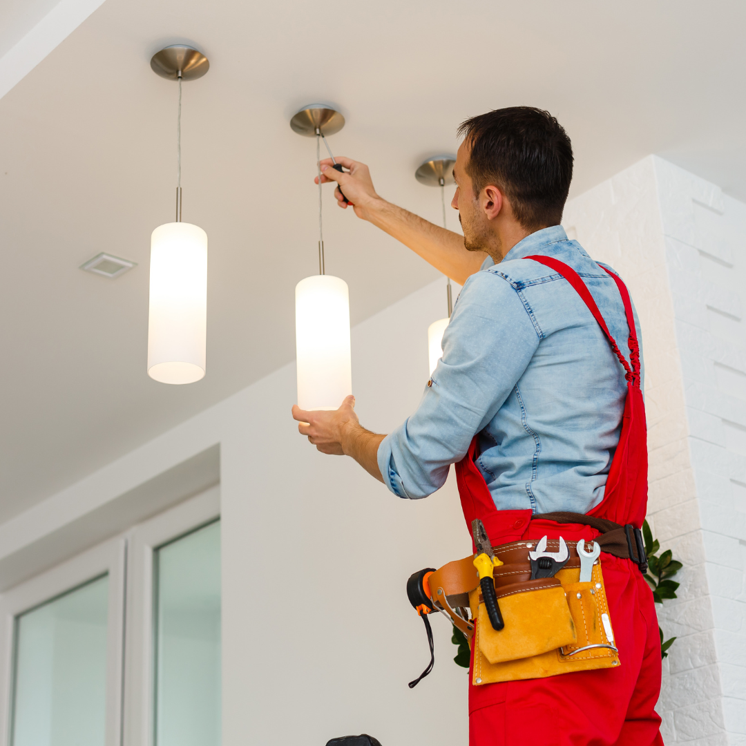 A man in red overalls is fixing a light fixture