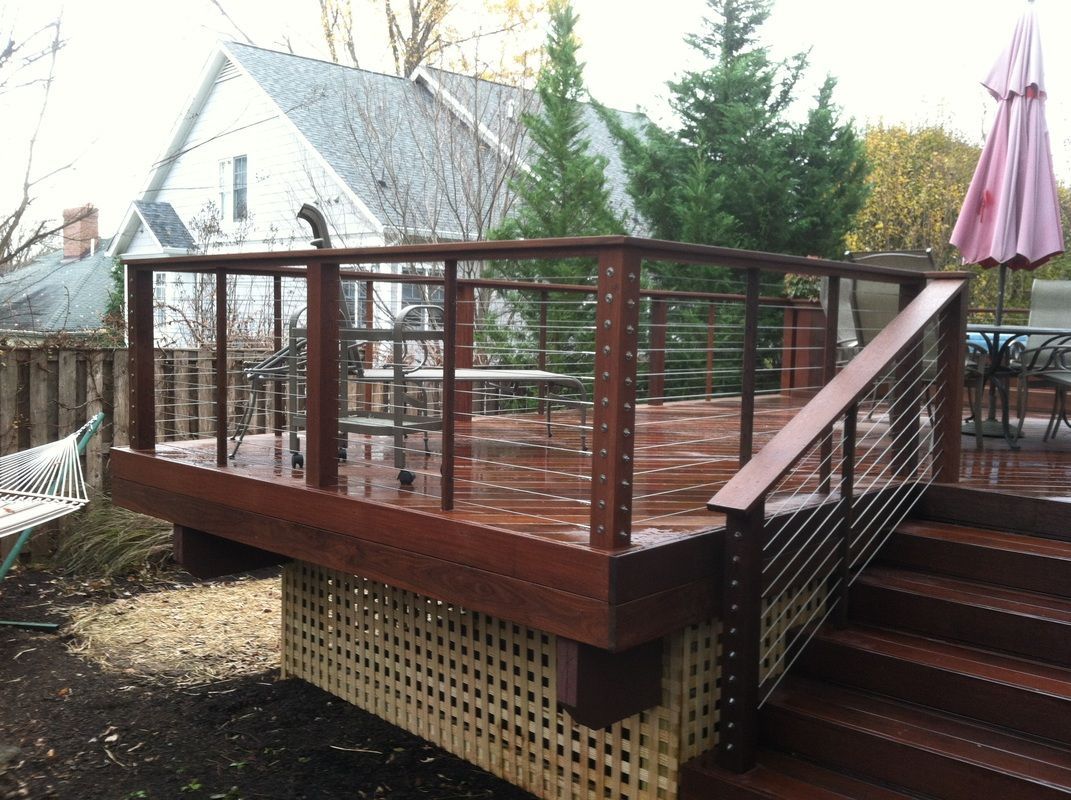Wooden deck with metal railing, stairs, and lattice skirting, with a house and trees in the background.