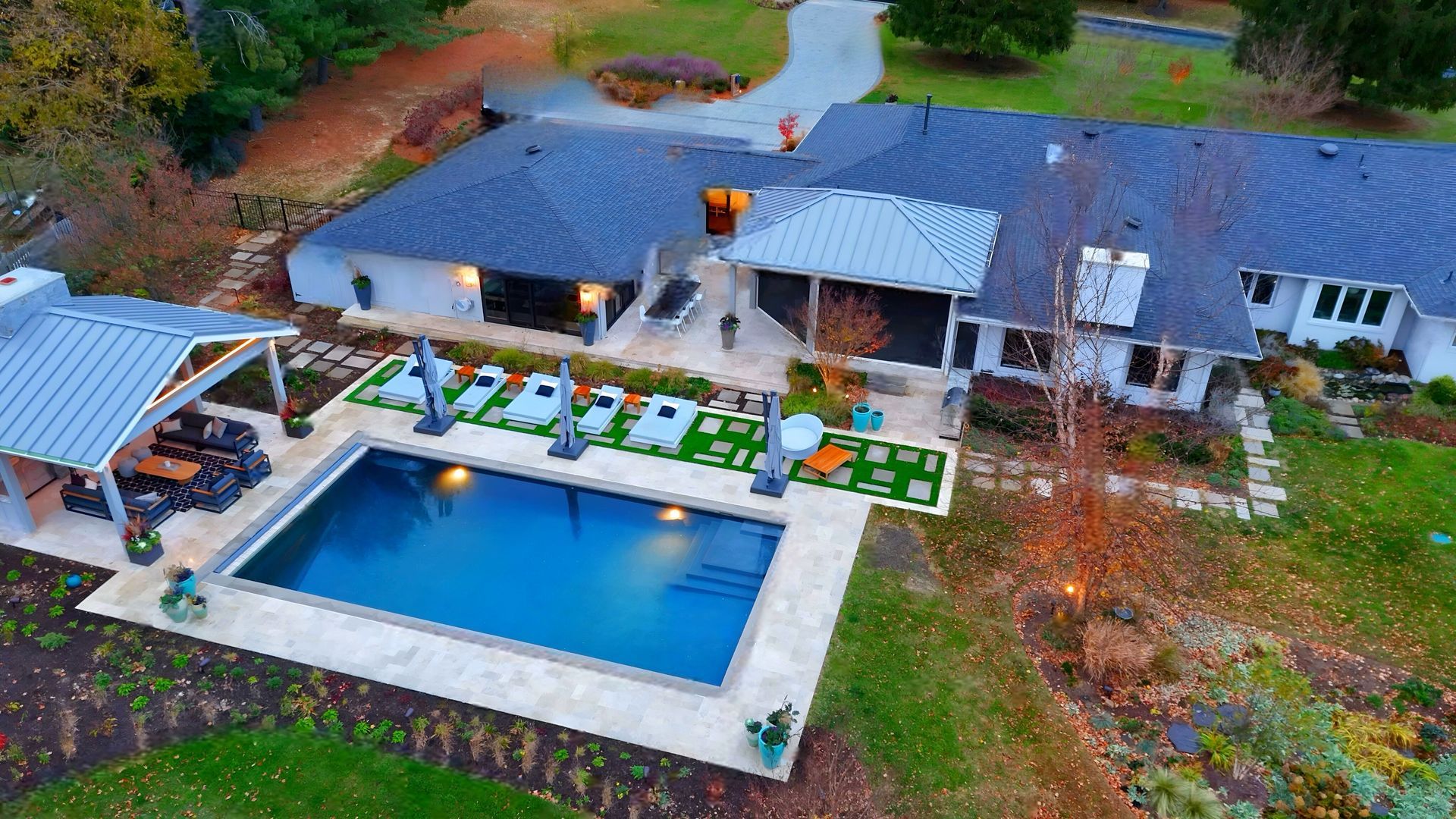 Aerial view of a home with a pool, patio, and outdoor dining area. The pool is blue and the house is white with a dark roof.