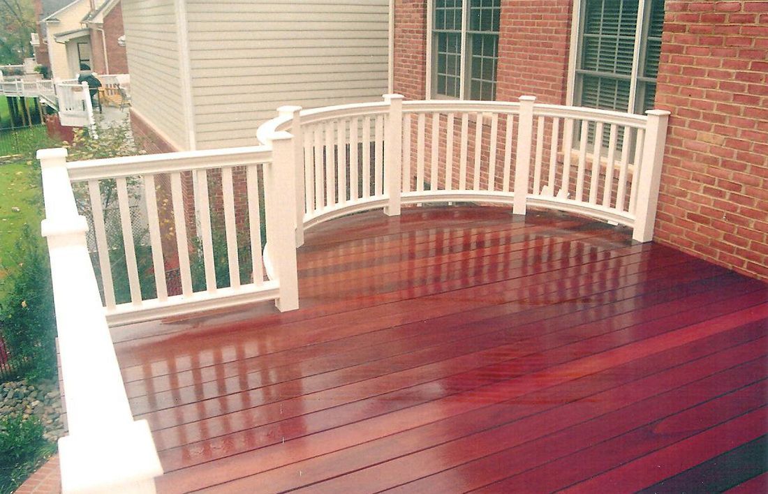 Wooden deck with red stain, white railing, curved section. Next to brick house.