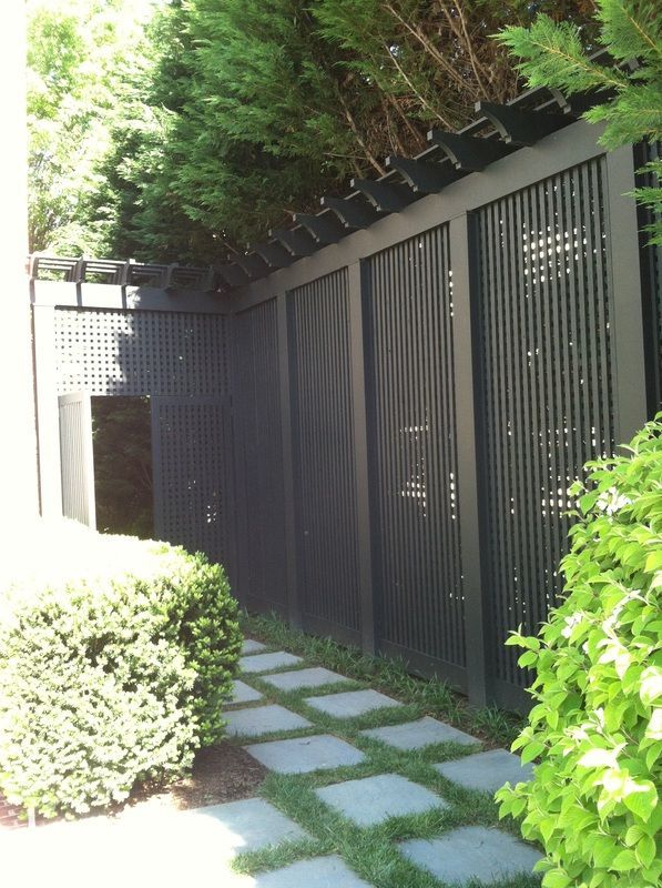 Dark wood fence with vertical and wavy slats, bordering a stone path with green foliage.