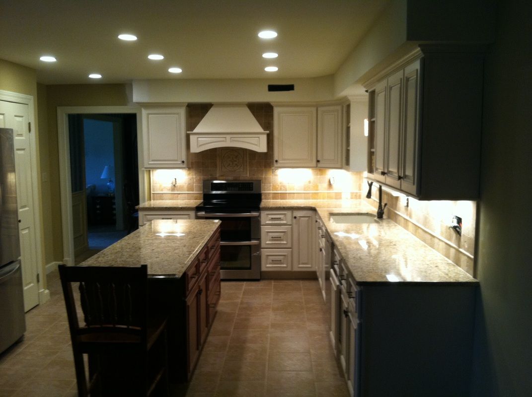 Kitchen with white cabinets, brown island, granite countertops, and recessed lighting.