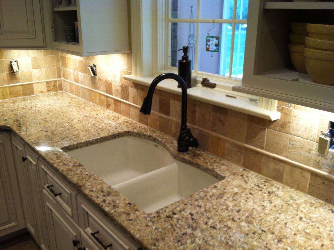 Kitchen counter with light granite, white sink, black faucet, and tan tile backsplash.