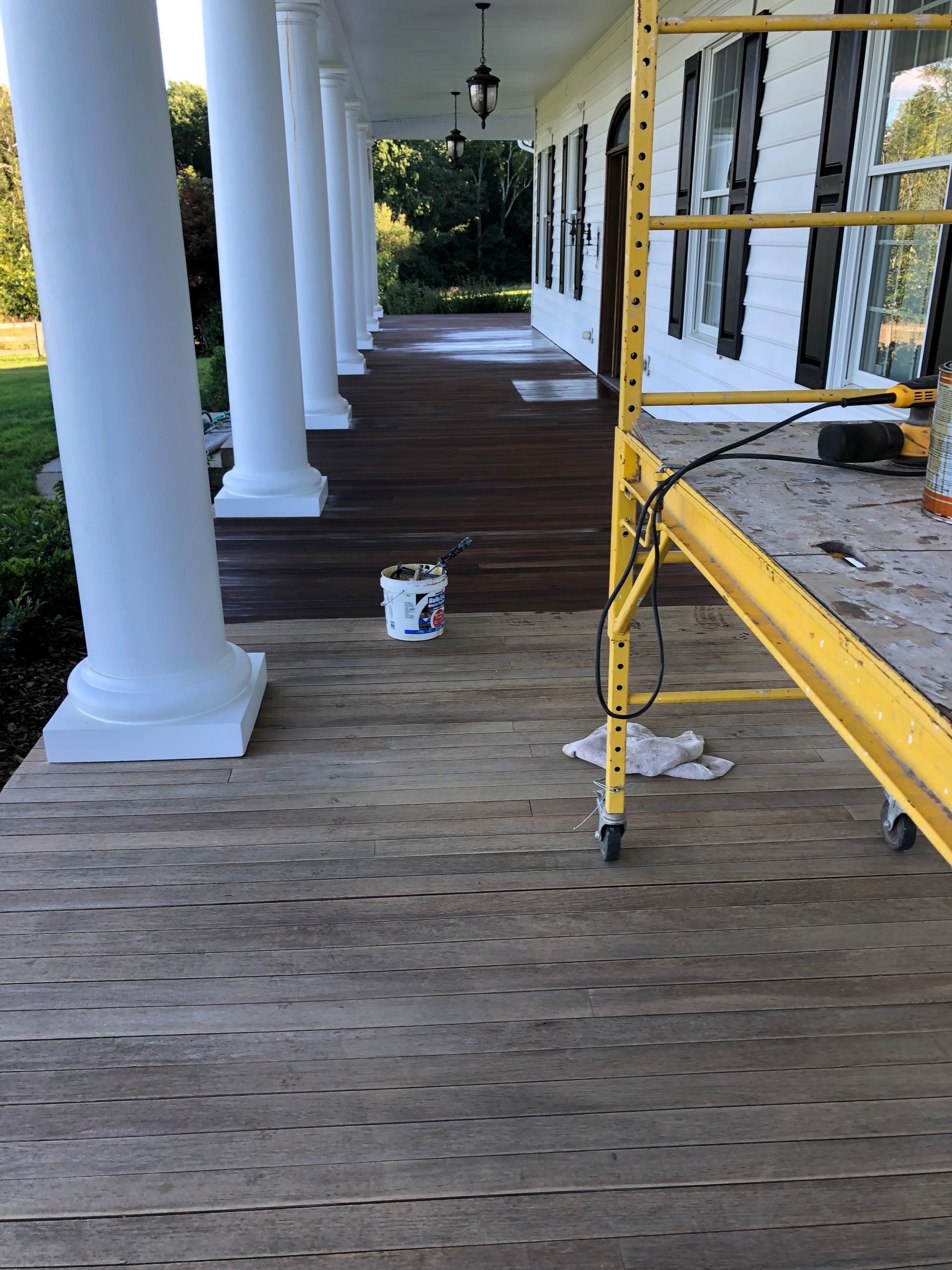 Wooden porch with white columns; a yellow scaffold stands nearby.