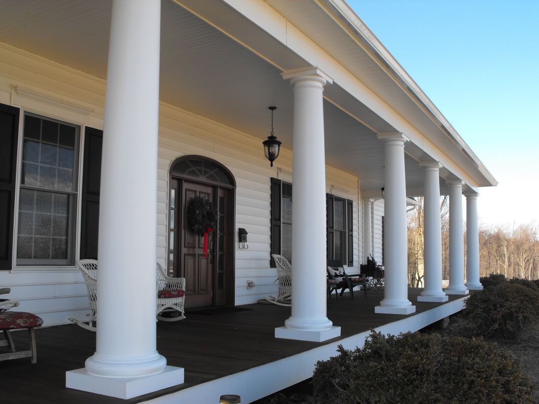 White house with large porch supported by tall columns, brown door.