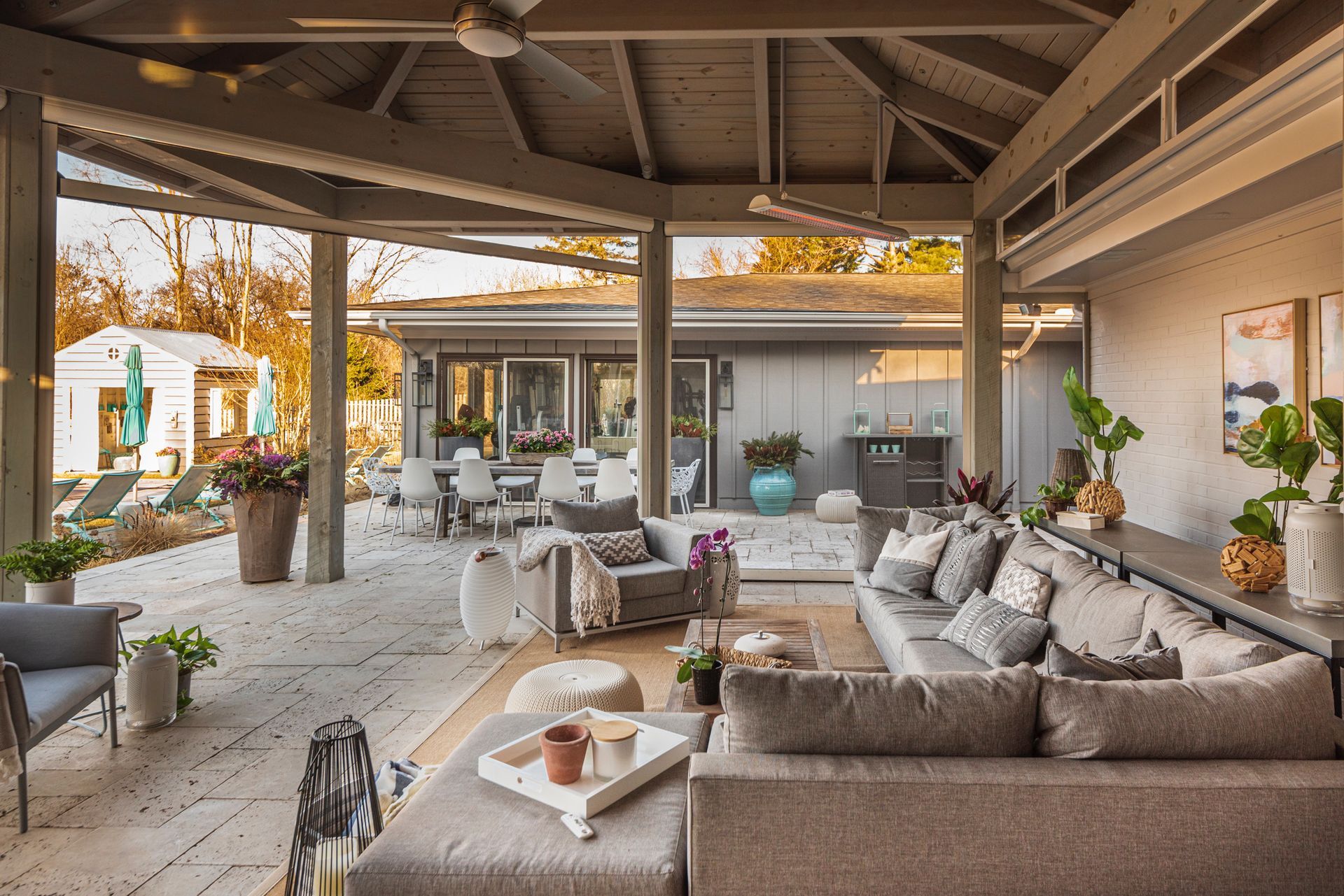 Outdoor living space with gray seating, overhead beams, and a view of a house and yard.