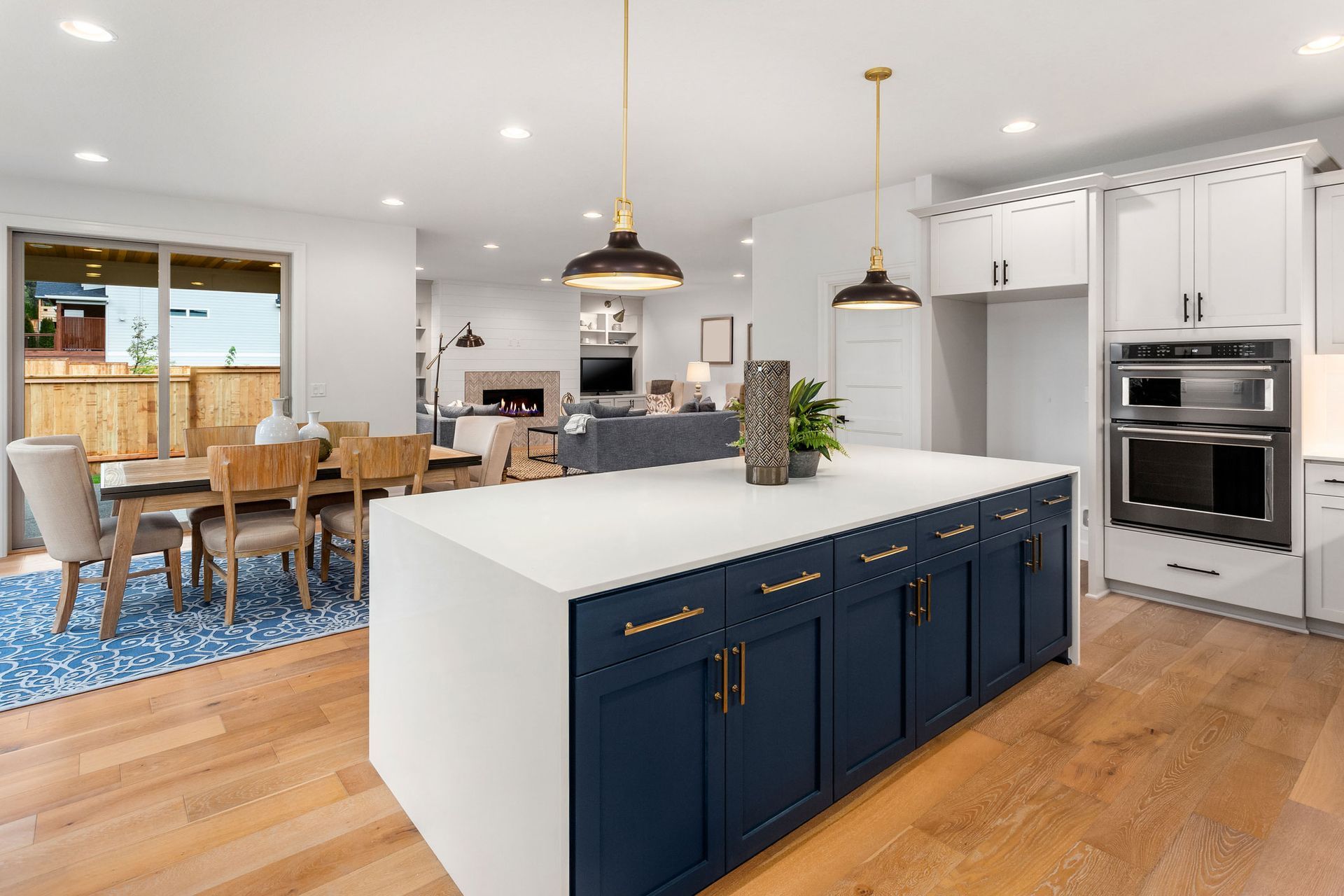 Modern kitchen with navy island, white countertops, and hardwood floors. Dining area visible.