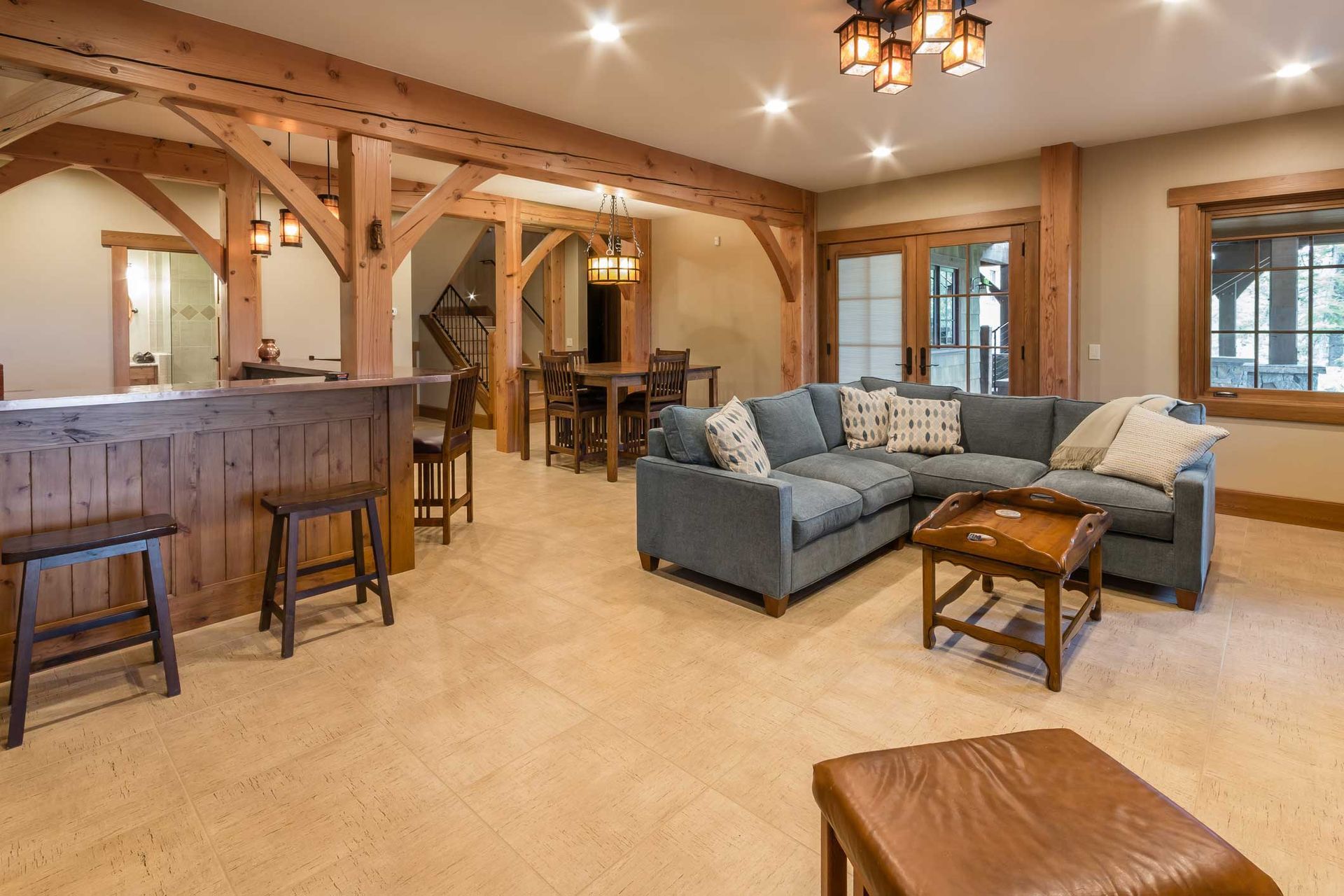 Spacious living area with wooden beams, bar, and blue sectional sofa, with light beige flooring.