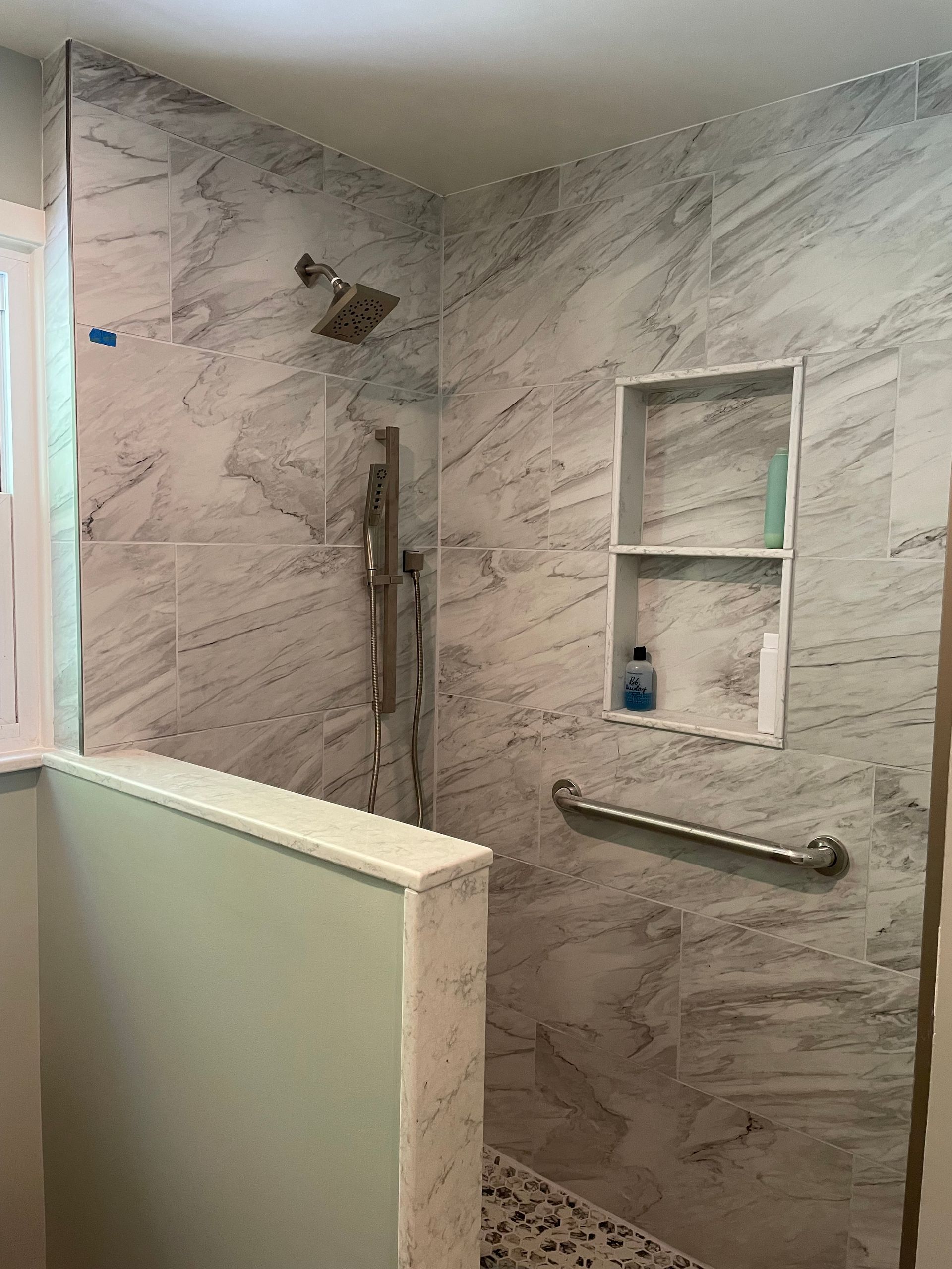 Newly remodeled shower with gray and white marble-look tiles, built-in shelves, and a grab bar.