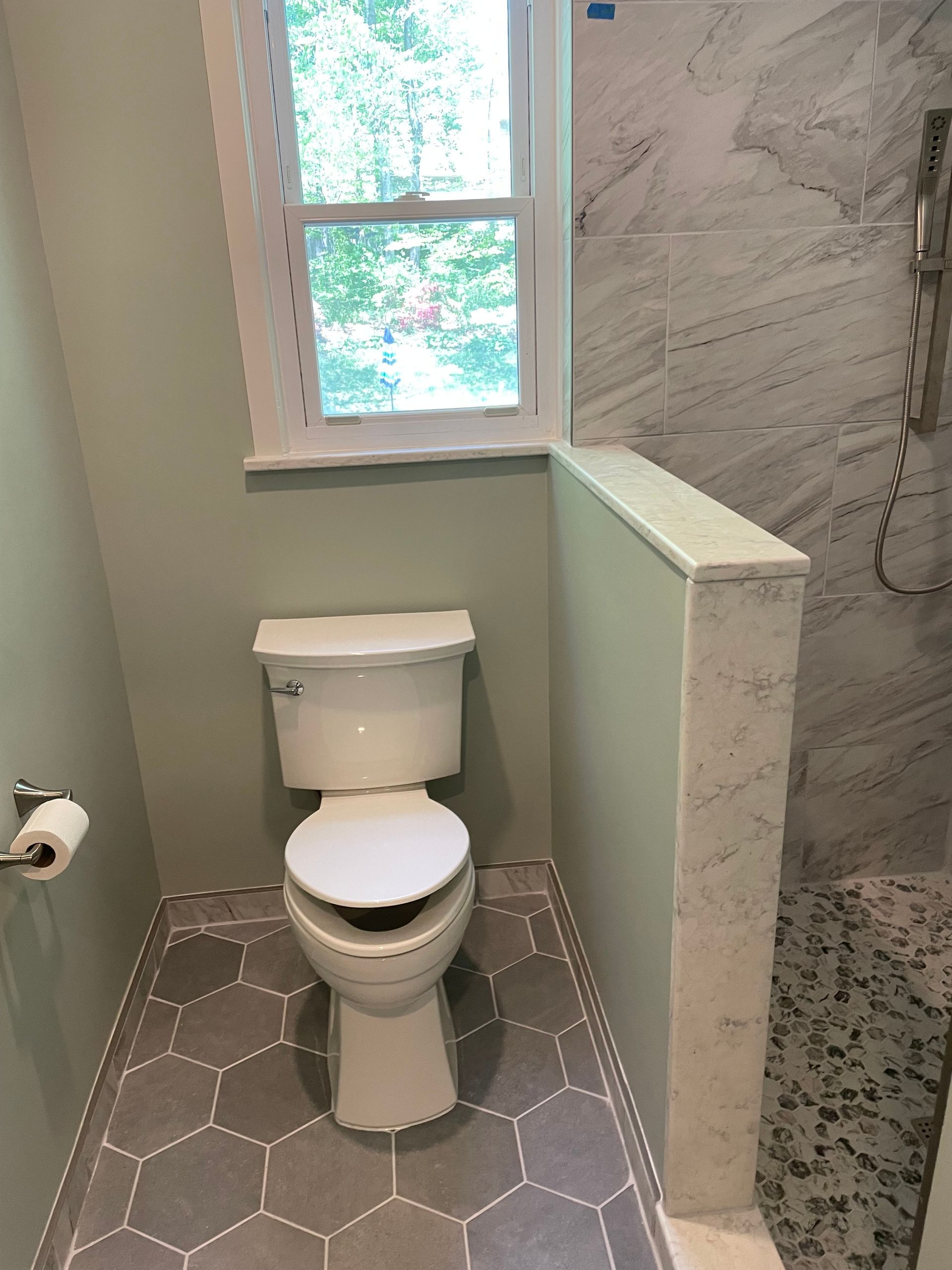 Bathroom with toilet, window, light green walls, and gray hexagonal tile floor.