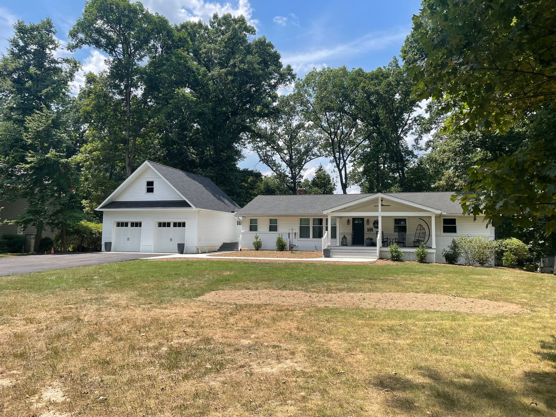 White house with attached garage, surrounded by trees and a green lawn under a blue sky.