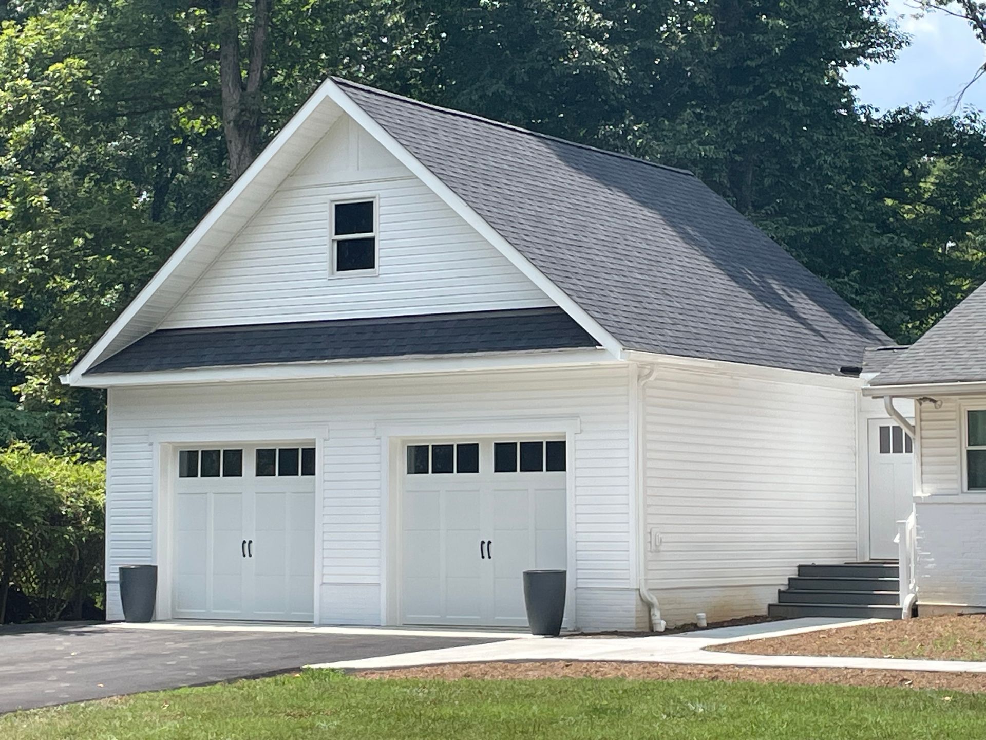 Two-car white garage with black roof, small window in gable, and dark planters.