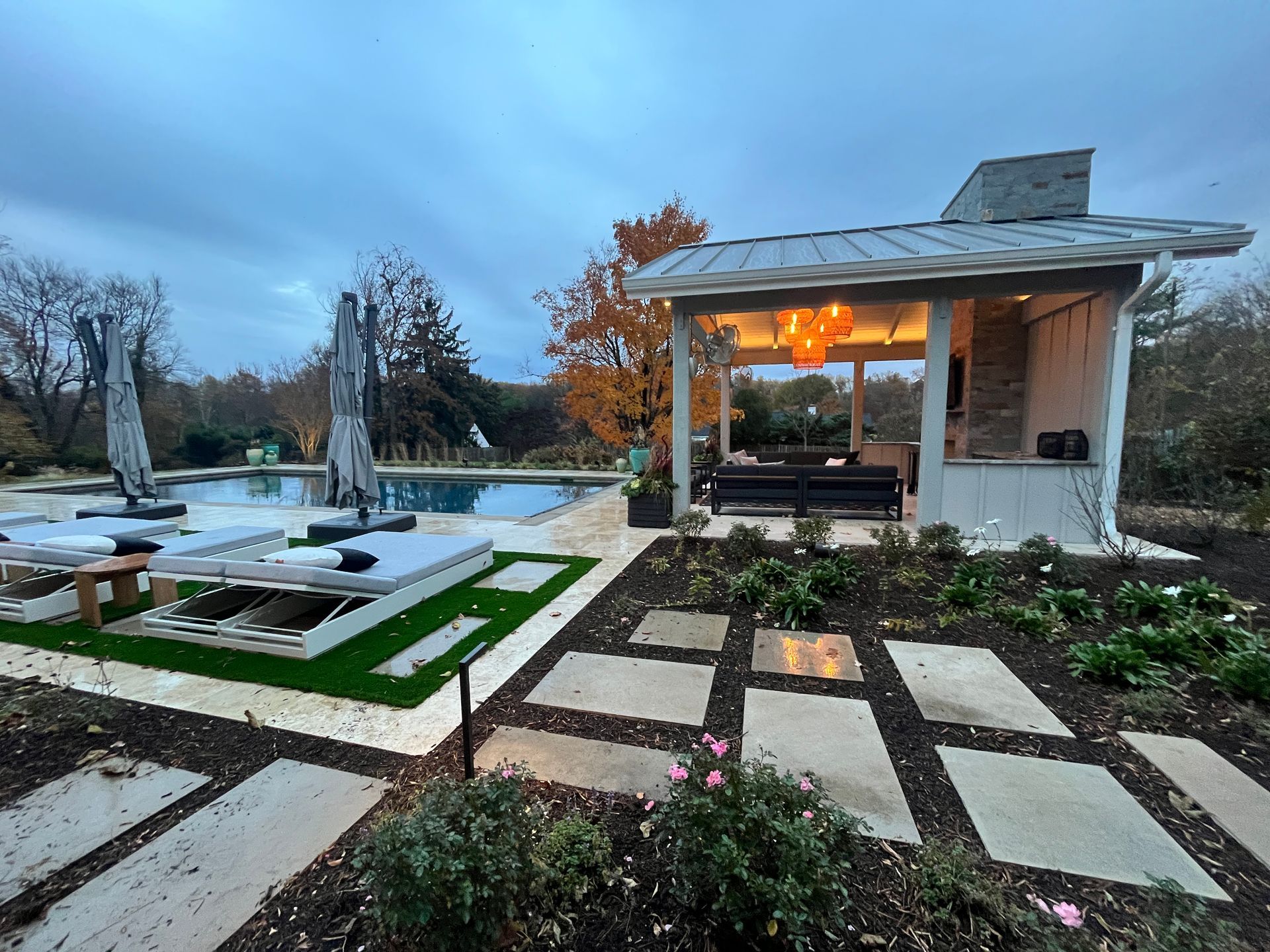 Poolside patio with a pool, lounge chairs, and a covered seating area at dusk.
